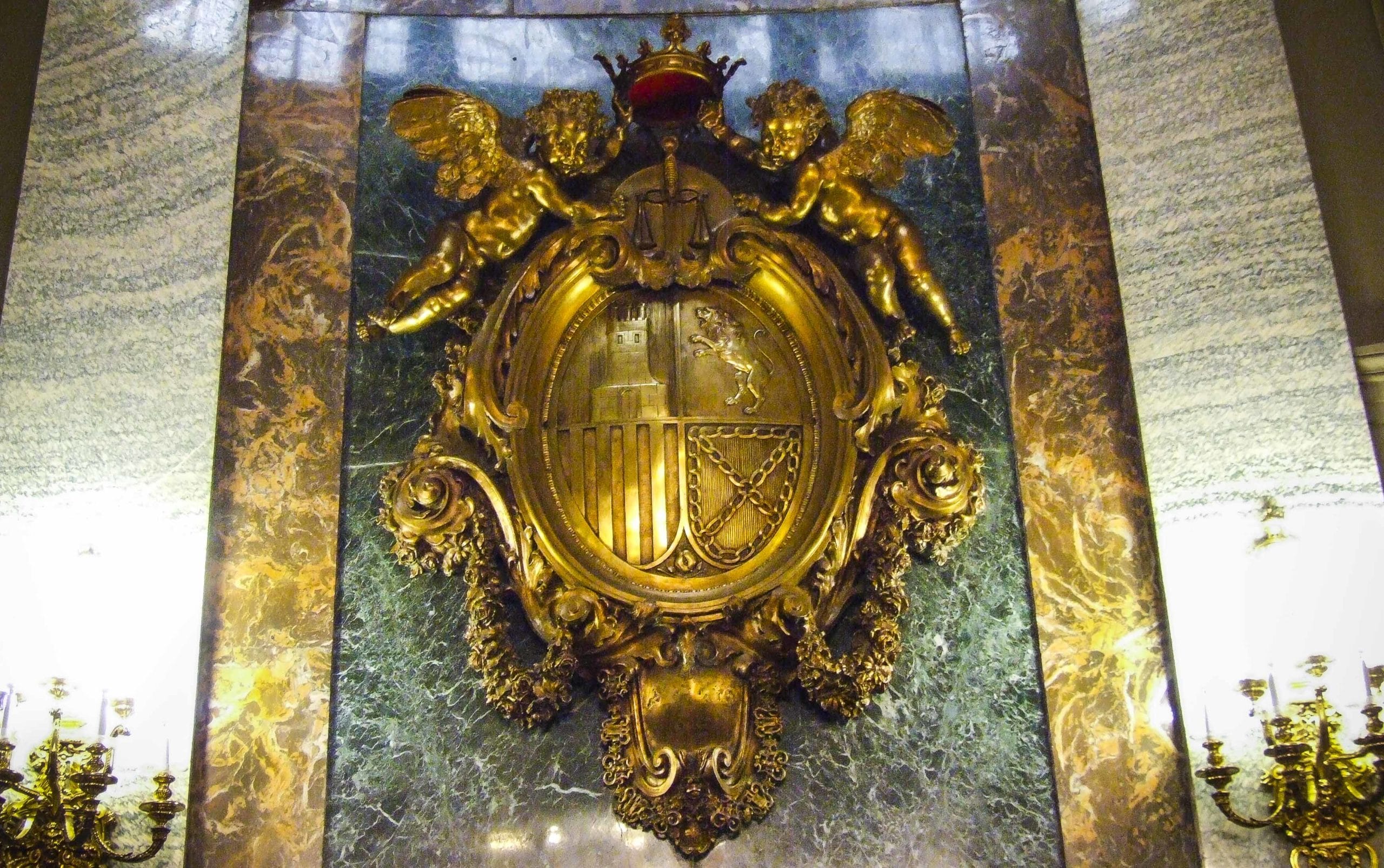 Este escudo, obra de Mariano Benlluire, no es el original; antes había un busto de Alfonso XIII que el ministro republicano, Álvaro de Albornoz, ordenó quitar y sustituir por el actual. Confilegal. 